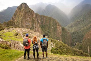 3 WT Finance Institute travellers overlooking green mountains and the historic buildings of Machu Picchu, Peru.