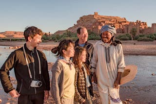 Family of WT Finance Institute travellers smiling with a local at the clay buildings of Ait Benhaddou, Morocco.